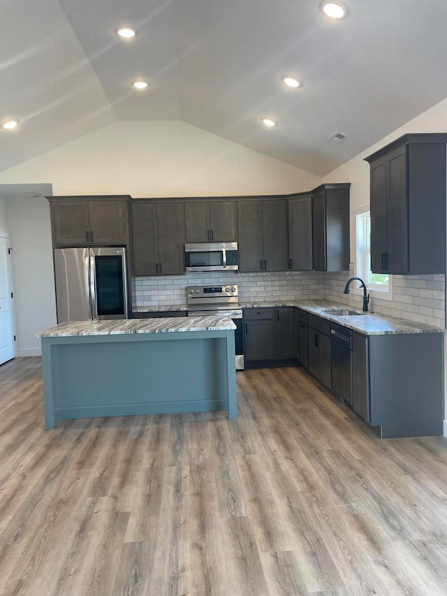 kitchen with vaulted ceiling, appliances with stainless steel finishes, light hardwood / wood-style floors, sink, and decorative backsplash