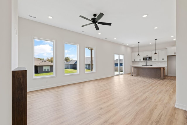 unfurnished living room with ceiling fan, sink, and light hardwood / wood-style floors