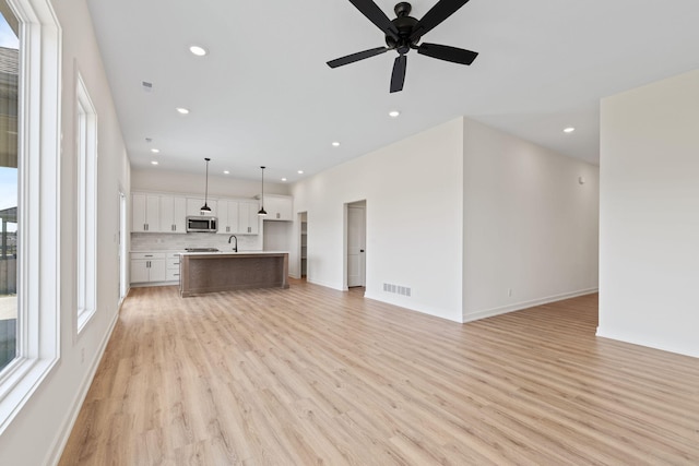 unfurnished living room with sink, light wood-type flooring, and ceiling fan