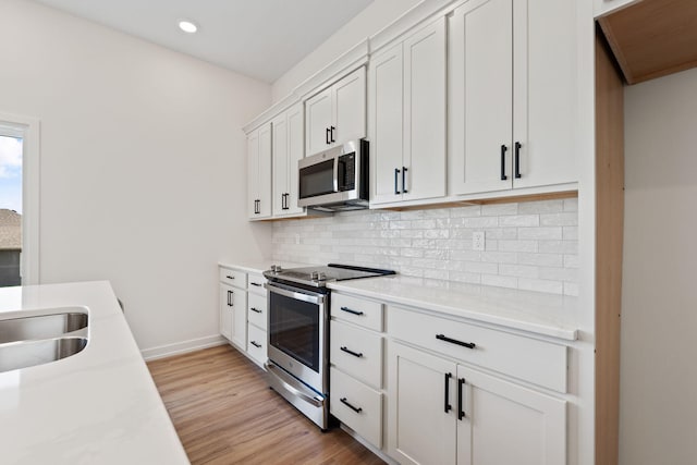 kitchen with light hardwood / wood-style floors, decorative backsplash, light stone countertops, white cabinets, and appliances with stainless steel finishes