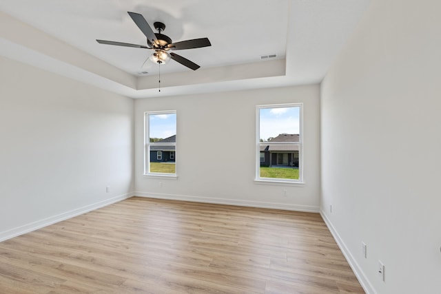 empty room with a raised ceiling, light hardwood / wood-style flooring, and ceiling fan