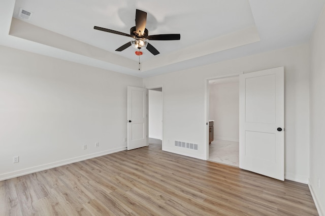 unfurnished bedroom with ceiling fan, light hardwood / wood-style flooring, ensuite bath, and a raised ceiling