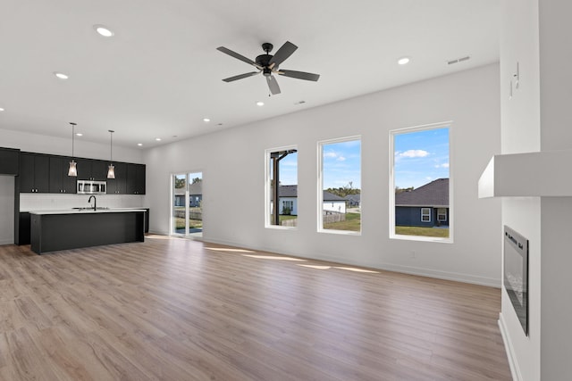 unfurnished living room featuring ceiling fan, sink, and light hardwood / wood-style floors