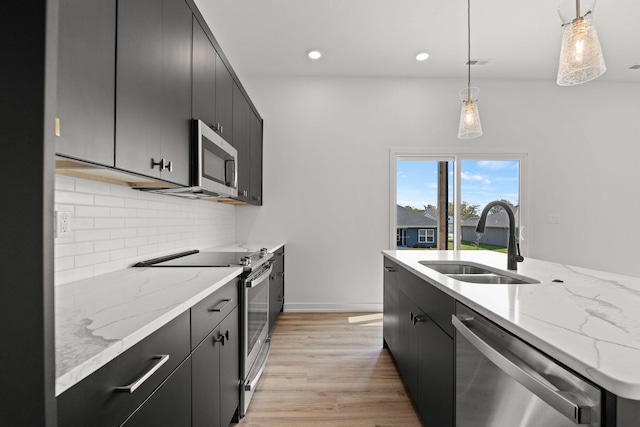 kitchen with stainless steel appliances, sink, light hardwood / wood-style floors, decorative light fixtures, and backsplash