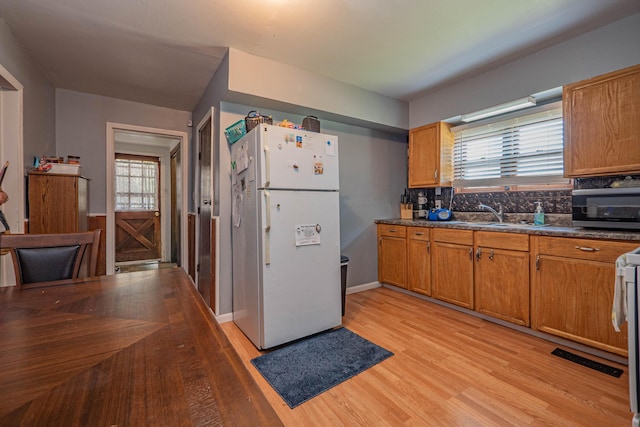 kitchen with backsplash, white refrigerator, sink, light wood-type flooring, and range