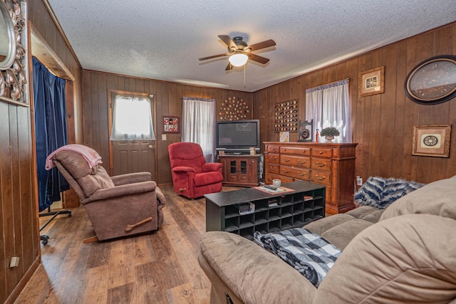 living room with ceiling fan, wood walls, dark hardwood / wood-style flooring, and a textured ceiling