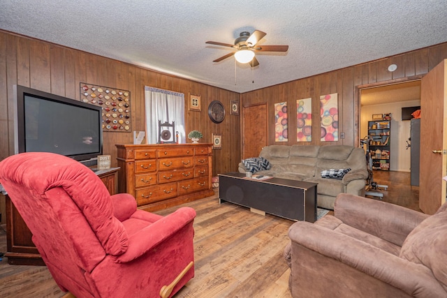 living room featuring ceiling fan, wooden walls, hardwood / wood-style floors, and a textured ceiling