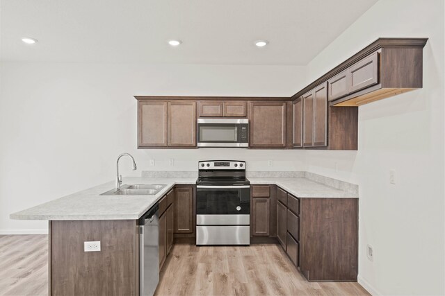 kitchen with dark brown cabinetry, sink, stainless steel appliances, kitchen peninsula, and light hardwood / wood-style floors