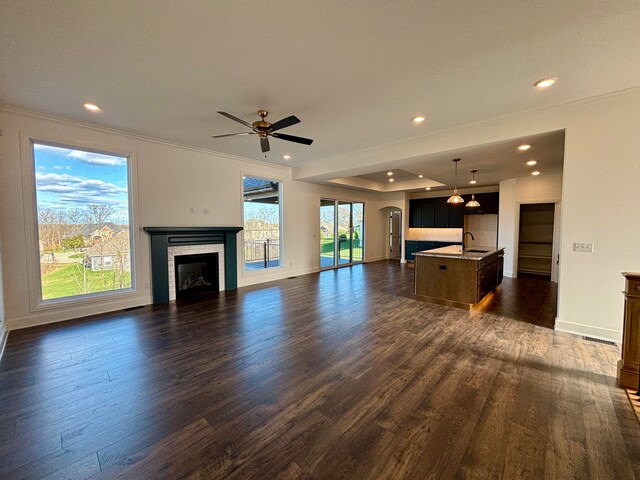 unfurnished living room with dark wood-style flooring, a fireplace, a sink, baseboards, and crown molding