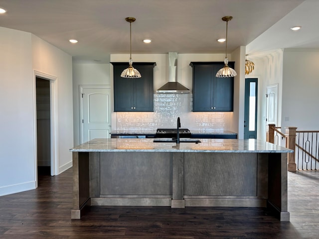 kitchen with a kitchen island with sink, light stone counters, wall chimney range hood, and decorative light fixtures