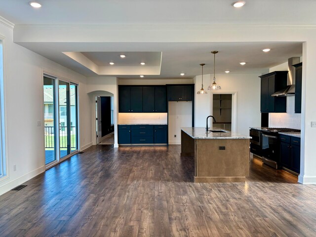 kitchen with arched walkways, decorative light fixtures, stainless steel range with gas stovetop, wall chimney exhaust hood, and a center island with sink