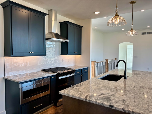 kitchen with arched walkways, stainless steel appliances, a sink, wall chimney range hood, and light stone countertops