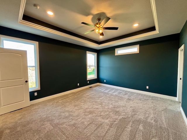 unfurnished room featuring a tray ceiling, light colored carpet, and baseboards