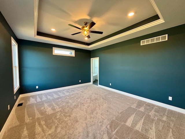 carpeted spare room featuring a tray ceiling, visible vents, and baseboards