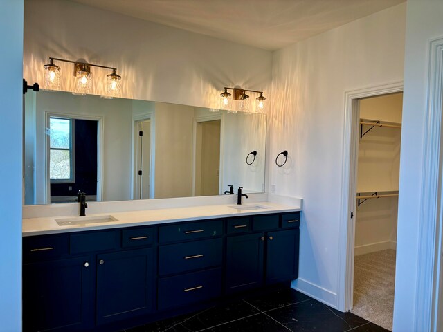 bathroom with a spacious closet, double vanity, a sink, and baseboards