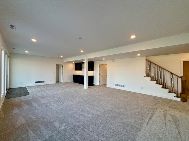 unfurnished living room with visible vents, baseboards, light colored carpet, stairway, and recessed lighting