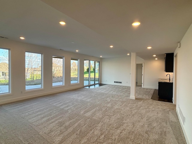 unfurnished living room with baseboards, visible vents, light colored carpet, a sink, and recessed lighting