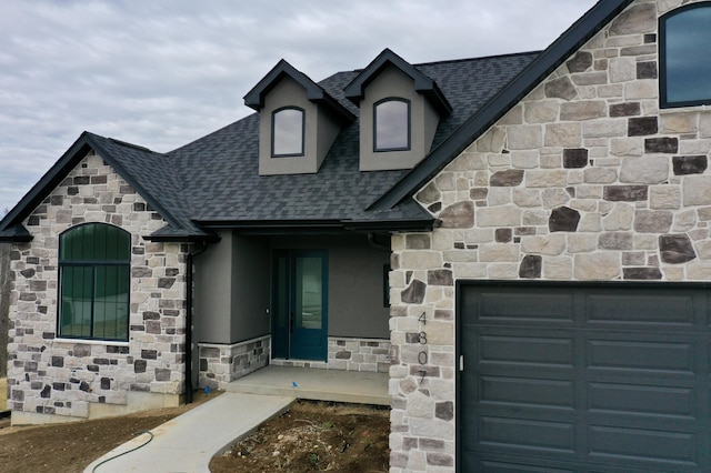 view of front of property featuring a garage, stone siding, and roof with shingles