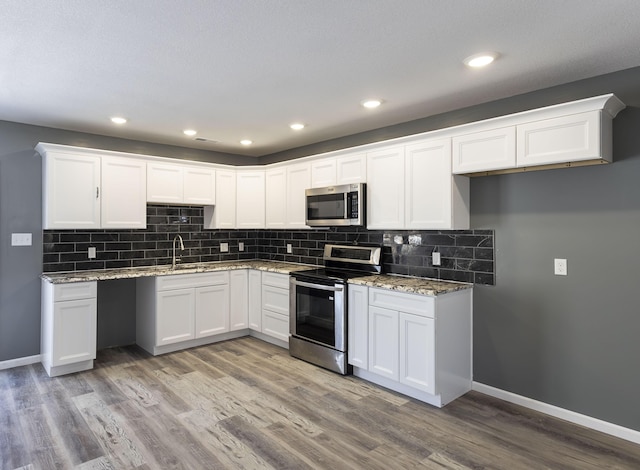 kitchen with stainless steel appliances, white cabinets, light stone countertops, and light hardwood / wood-style flooring