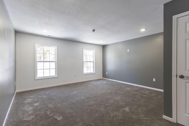 spare room with a textured ceiling and dark carpet