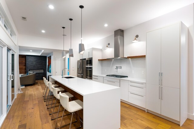 kitchen featuring sink, a center island with sink, white cabinets, and wall chimney exhaust hood