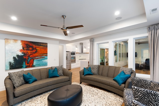 living room with a tray ceiling, light hardwood / wood-style flooring, and ceiling fan