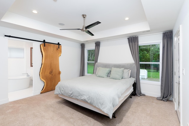 carpeted bedroom with ceiling fan, a raised ceiling, and a barn door