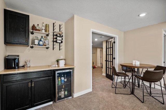 bar featuring beverage cooler, light colored carpet, and a textured ceiling