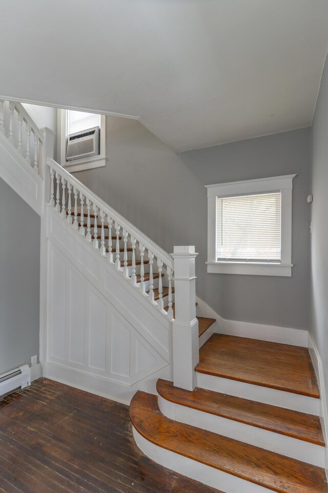 staircase featuring lofted ceiling, baseboard heating, a wall mounted AC, baseboards, and hardwood / wood-style flooring