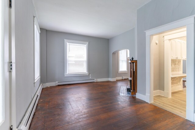 empty room with a baseboard heating unit, arched walkways, hardwood / wood-style floors, and baseboard heating