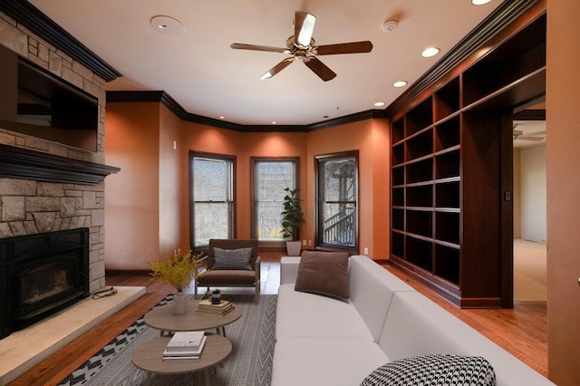 living area featuring a stone fireplace, recessed lighting, wood finished floors, and crown molding