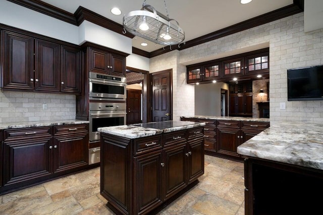 kitchen with crown molding, stone tile flooring, double oven, glass insert cabinets, and light stone countertops