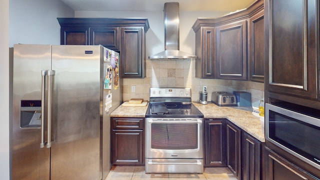 kitchen featuring backsplash, wall chimney range hood, light stone countertops, dark brown cabinetry, and stainless steel appliances