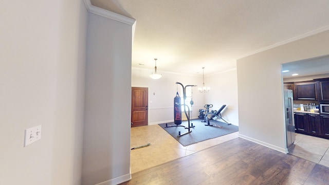 workout area with light hardwood / wood-style flooring, an inviting chandelier, and ornamental molding