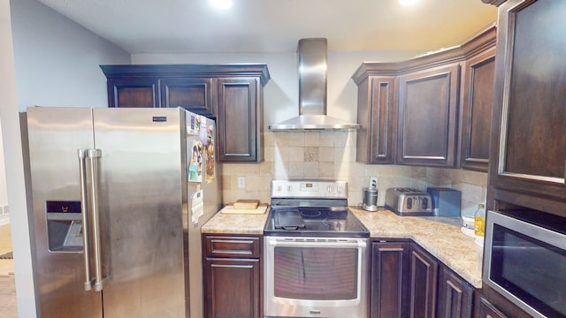 kitchen featuring dark brown cabinetry, wall chimney range hood, appliances with stainless steel finishes, and tasteful backsplash