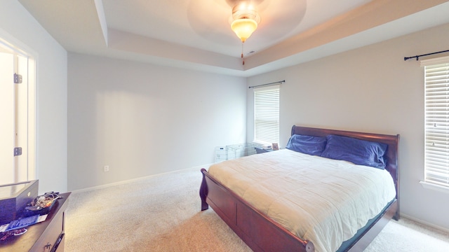 bedroom with light carpet, a tray ceiling, and ceiling fan