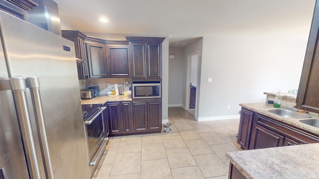 kitchen featuring stove, sink, light tile patterned floors, built in microwave, and high end fridge