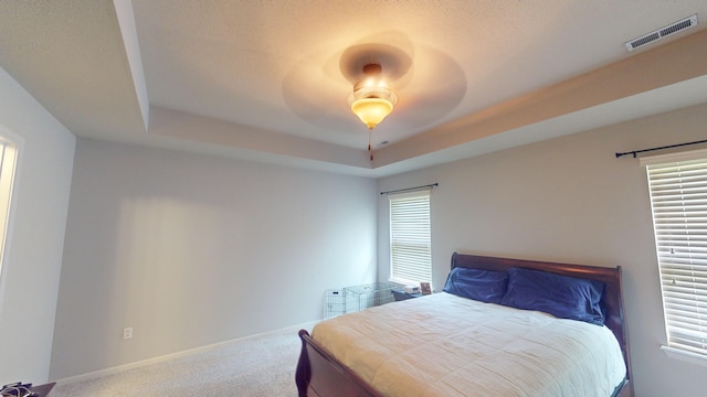 carpeted bedroom featuring a raised ceiling, multiple windows, and ceiling fan