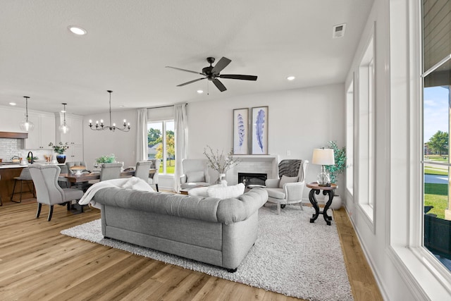 living room with ceiling fan with notable chandelier and light hardwood / wood-style flooring