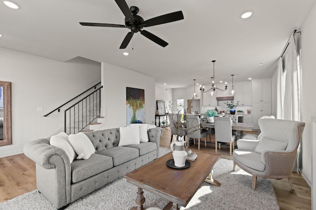 living room with light wood-type flooring and ceiling fan with notable chandelier