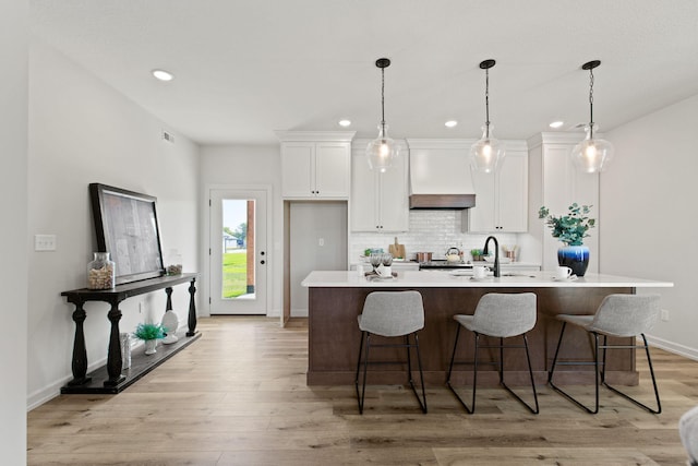 kitchen featuring light hardwood / wood-style floors, white cabinetry, an island with sink, premium range hood, and sink