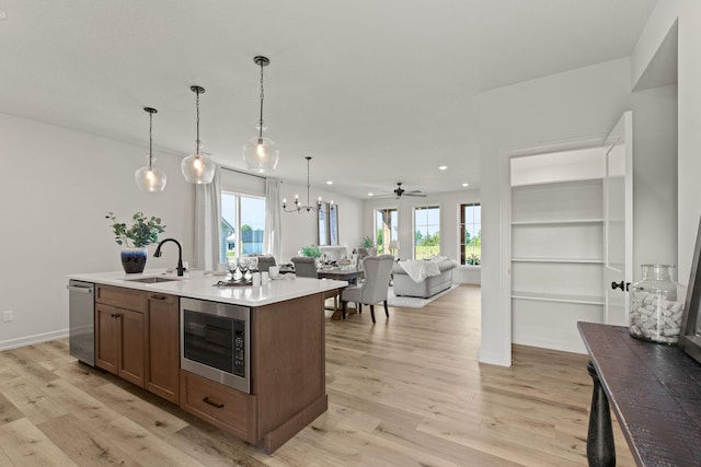 kitchen with light hardwood / wood-style floors, sink, hanging light fixtures, a center island with sink, and appliances with stainless steel finishes