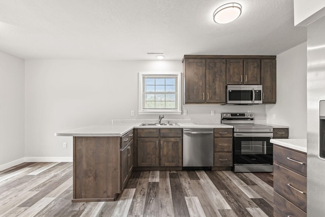 kitchen featuring wood-type flooring, sink, dark brown cabinetry, kitchen peninsula, and stainless steel appliances