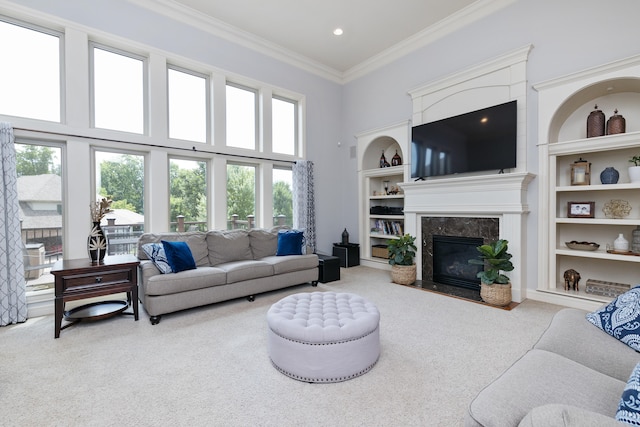 carpeted living room with built in shelves, a towering ceiling, a fireplace, and ornamental molding