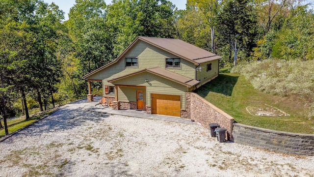 view of front of home featuring a garage, a front yard, stone siding, and gravel driveway