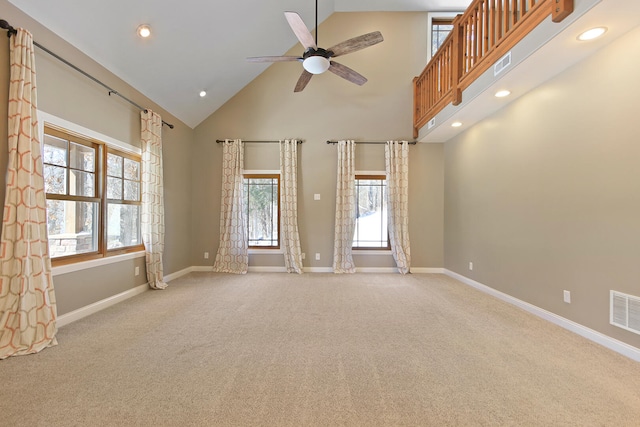 empty room with light colored carpet, visible vents, a ceiling fan, high vaulted ceiling, and baseboards