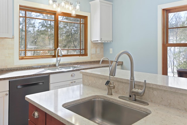 kitchen with black dishwasher, decorative backsplash, white cabinets, and a sink