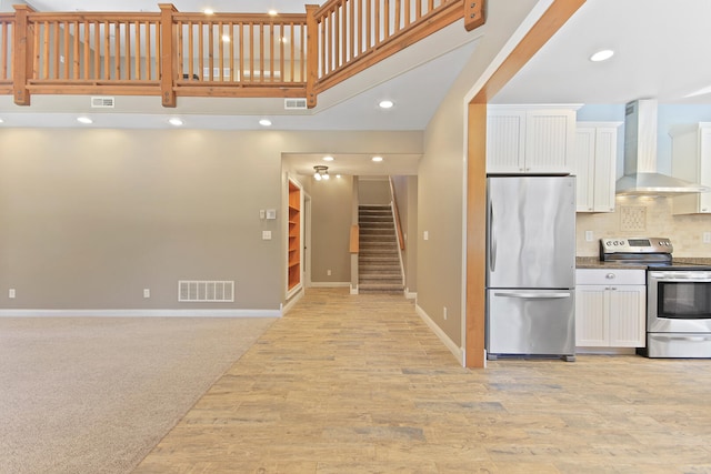 kitchen featuring wall chimney range hood, white cabinetry, visible vents, and appliances with stainless steel finishes