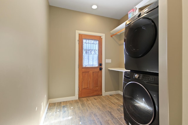 clothes washing area with laundry area, light wood finished floors, stacked washer / dryer, and baseboards