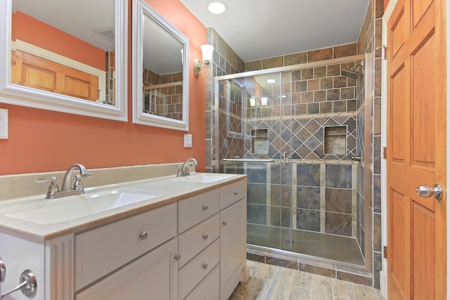 full bathroom with wood finish floors, a sink, a tile shower, and double vanity